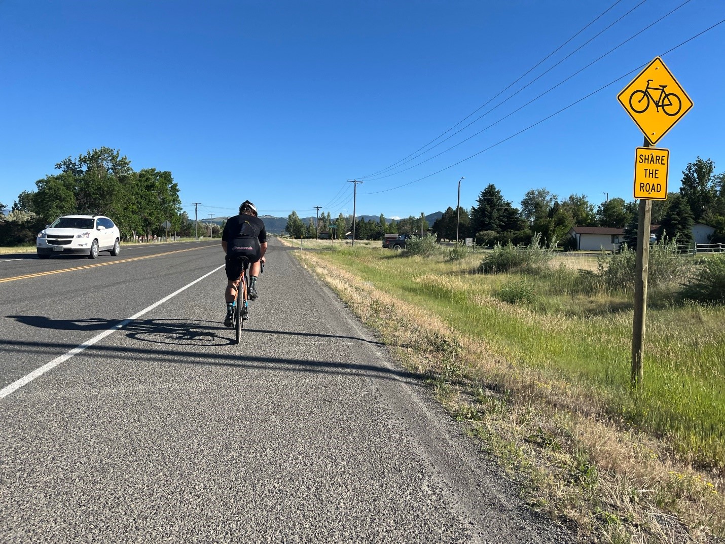 Bicyclist riding down shoulder of highway with a sign nearby that says Share The Road