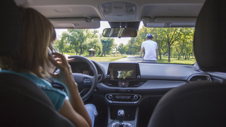View from inside a car where a driver is talking on her cell phone and there is a cyclist in front of her