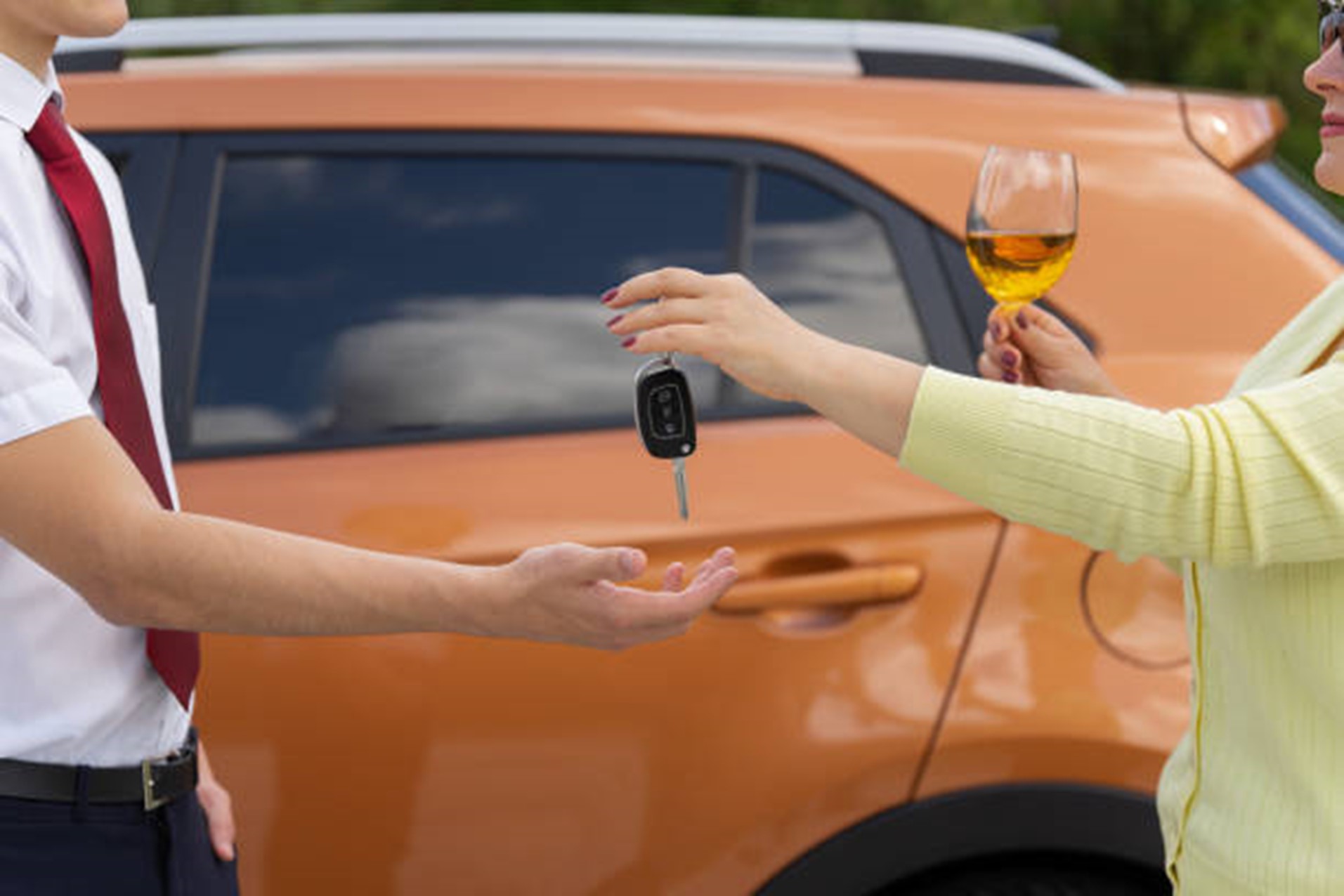 Women standing in front of her car, holding a wine glass, handing her keys to a man 
