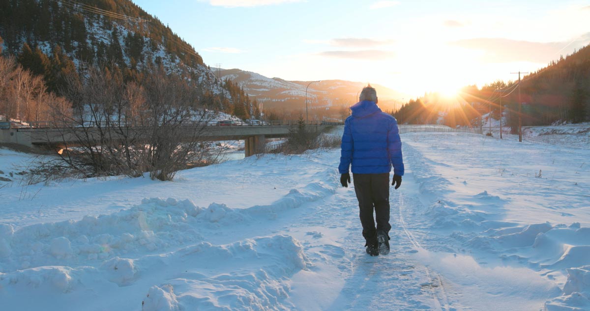 Man walking along snowy walking path towards a sunset in the mountains
