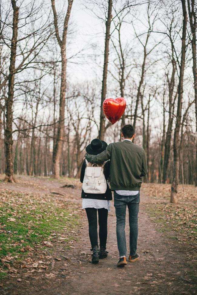 A couple walking along a dirt trail with a red heart balloon above them