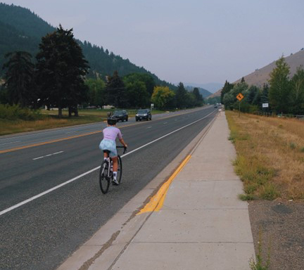 Bicyclist riding away down the highway towards mountains with hazy blue sky